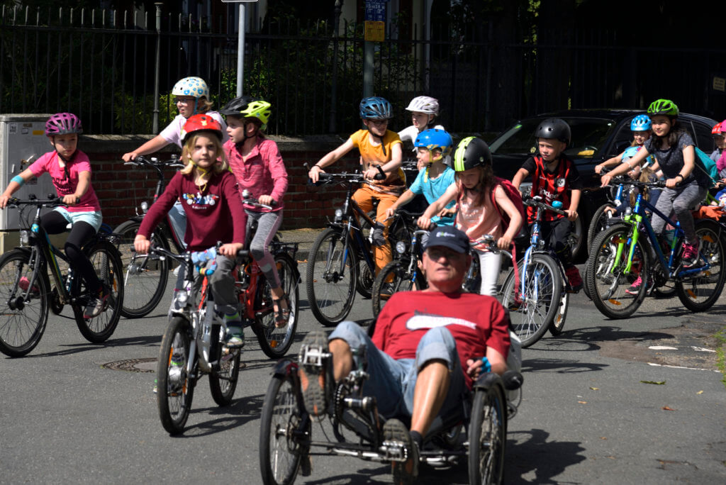 Ein Mann mit Liegerad führt die Kidical Mass an, viele Kinder fahren hinterher.
