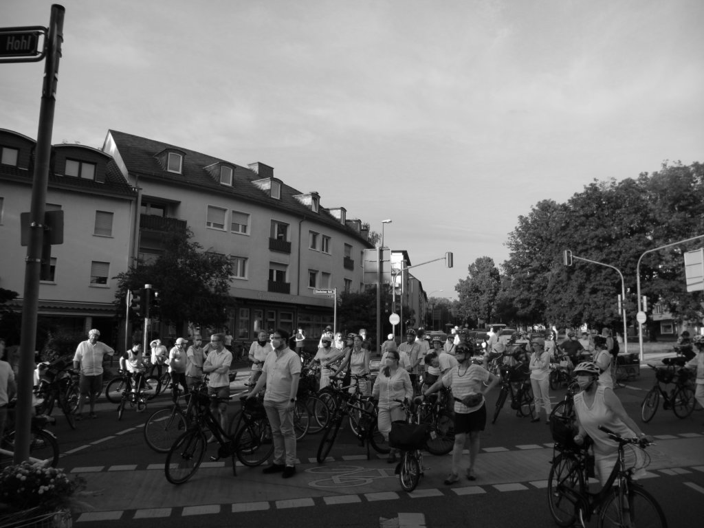 Die Teilnehmenden der Demonstration stehen zur Schlusskundgebung auf der Kreuzung am Ginnheimer Hohl; im Hintergrund die wartenden Autos.