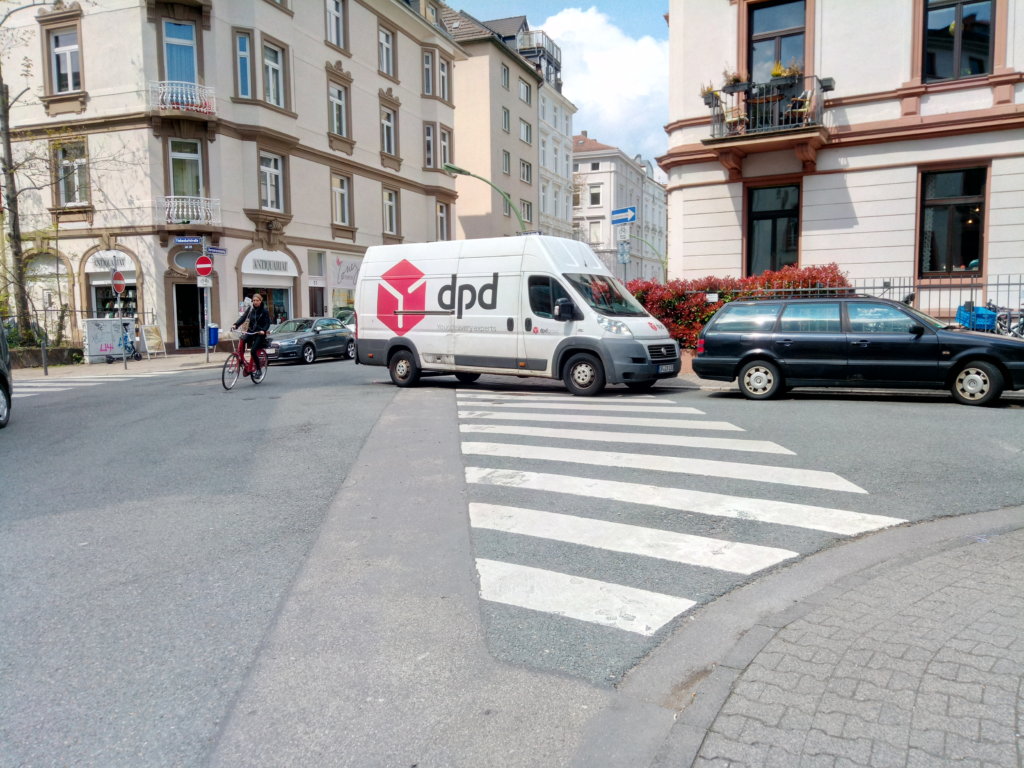 Foto einer kleinen Kreuzung in Frankfurt, wo die Probleme deutlich sichtbar werden: blockierte Sichtachsen und illegal zugeparkte Überwege.